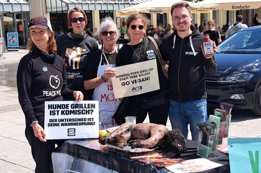 PETA Streetteam mit Schildern und Hundeatrappe auf einem Grill.