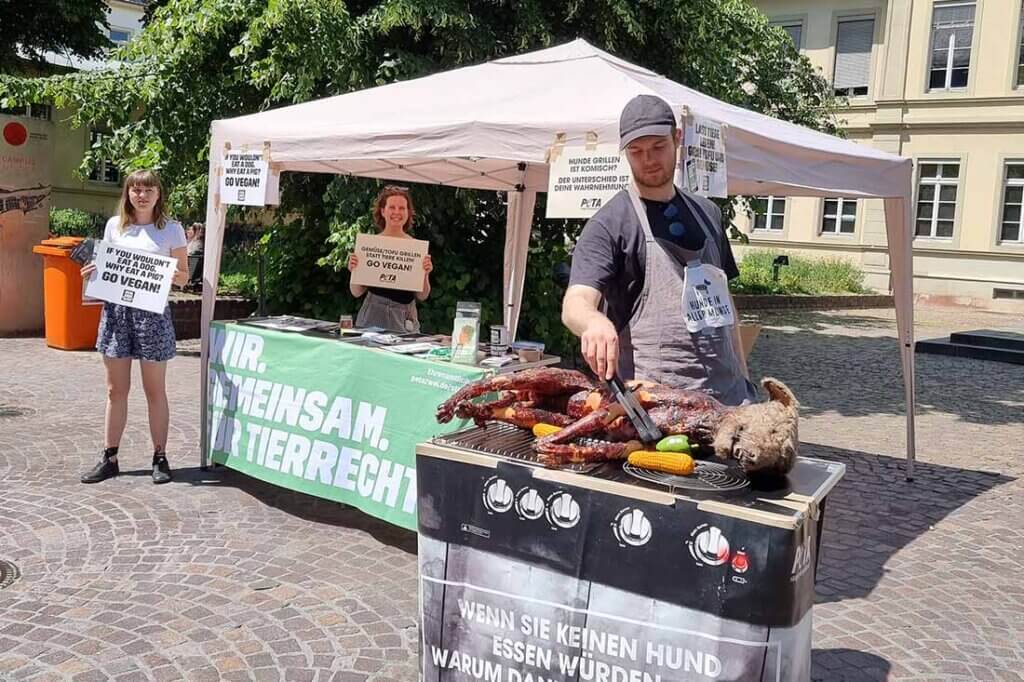 PETA Streetteam mit Schildern und Hundeatrappe auf einem Grill.