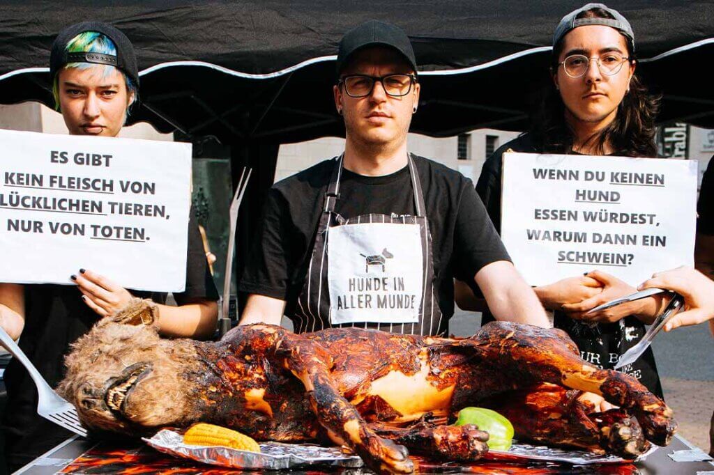 PETA Streetteam mit Schildern und Hundeatrappe auf einem Grill.