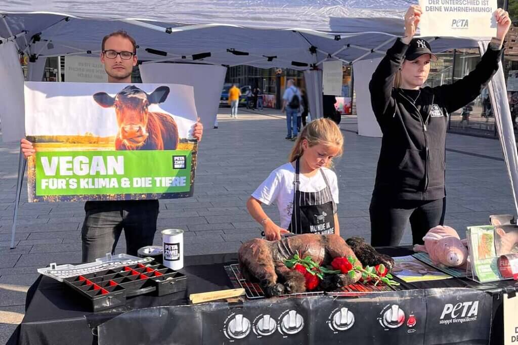 PETA Streetteam mit Schildern und Hundeatrappe auf einem Grill.