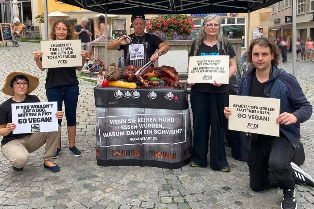 PETA Streetteam mit Schildern und Hundeatrappe auf einem Grill.