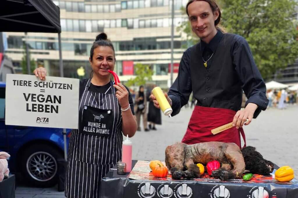 PETA Streetteam mit Schildern und Hundeatrappe auf einem Grill.