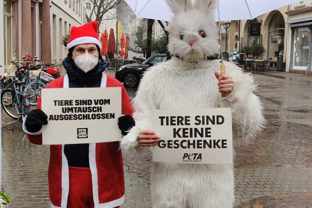 Person im Weihnachtsmannkostuem und eine Person im Hasenkostuem mit Schildern