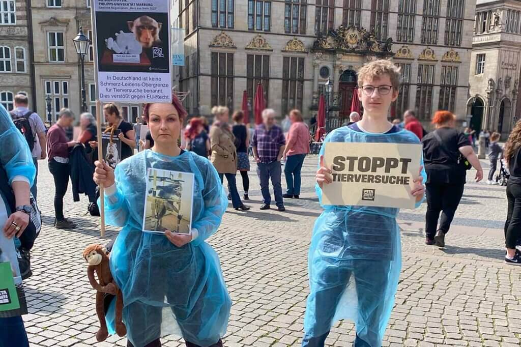 Demonstrierende in blauen Anzuegen gegen Tierversuche stehen mit Schildern und Bannern auf einer Strasse.