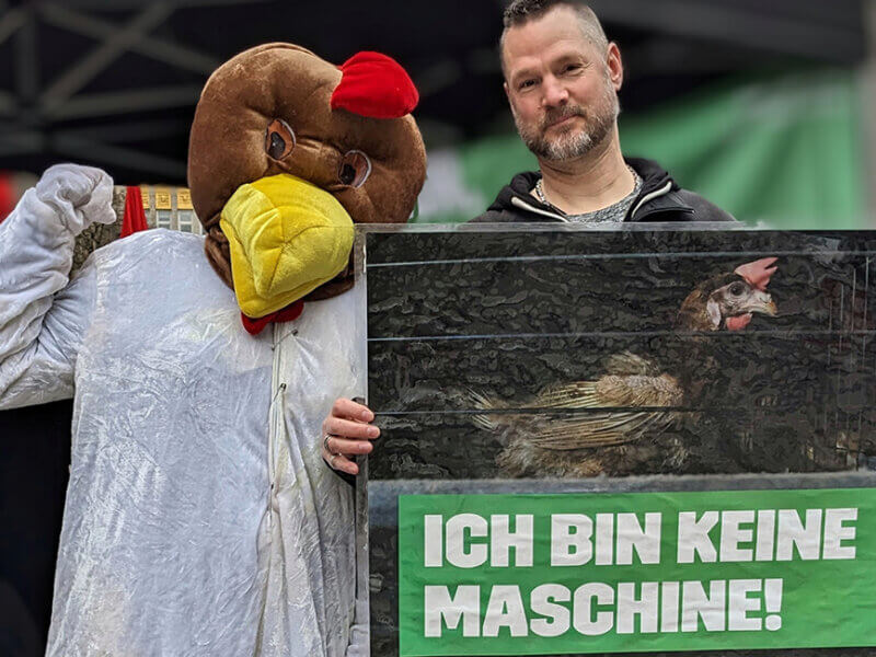 Mann mit Schild steht neben einer Person im Huenerkostuem.