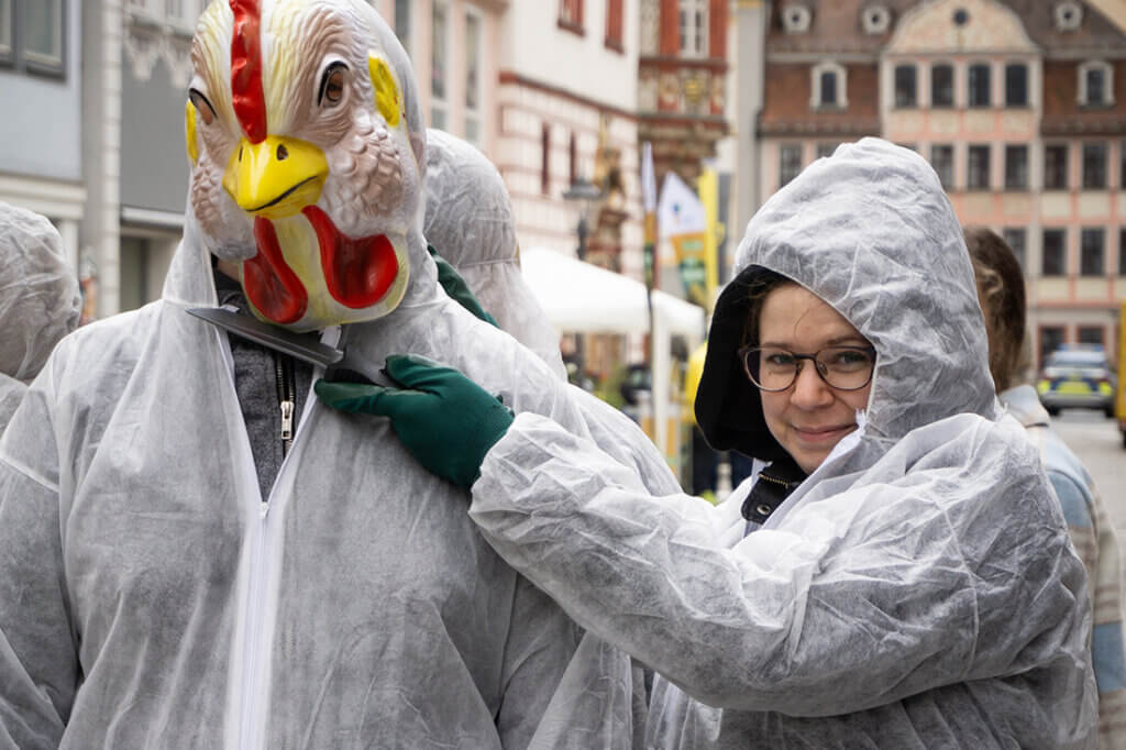 Aktivisten in Huehnerkostuemen stehen auf der Strasse.