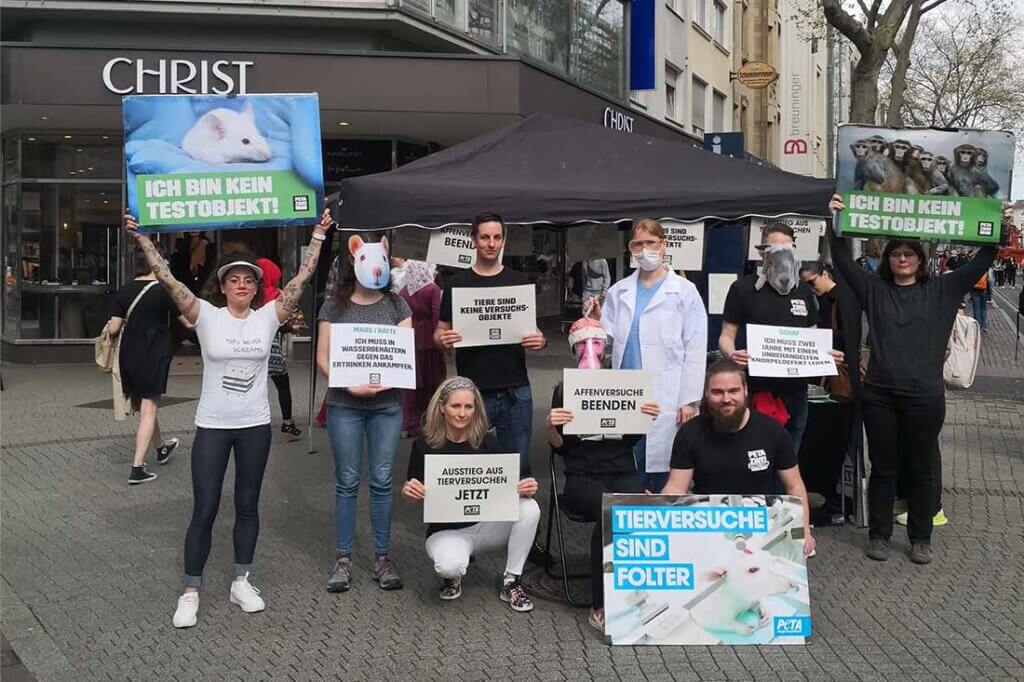 Demonstrierende gegen Tierversuche stehen mit Schildern und Bannern auf einer Strasse.