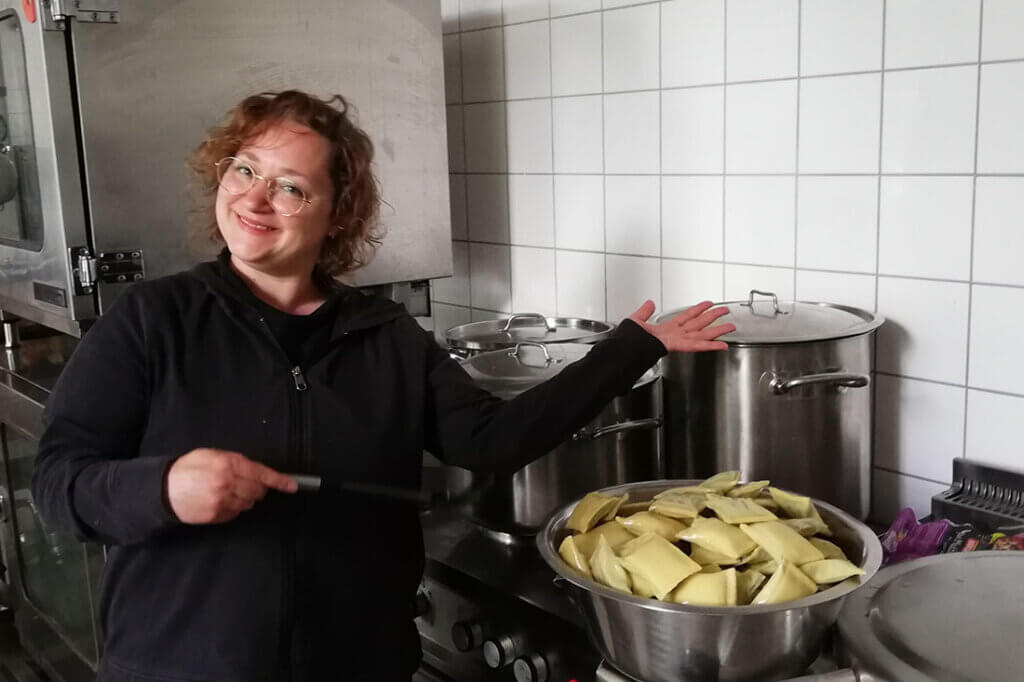 Frau steht am Herd vor verschiedenen Kochtoepfen und einer Schuessel Maultaschen.