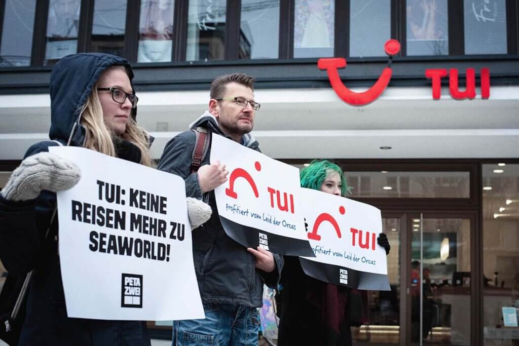 Menschen protestieren gegen TUI vor einem TUI Reisebüro.
