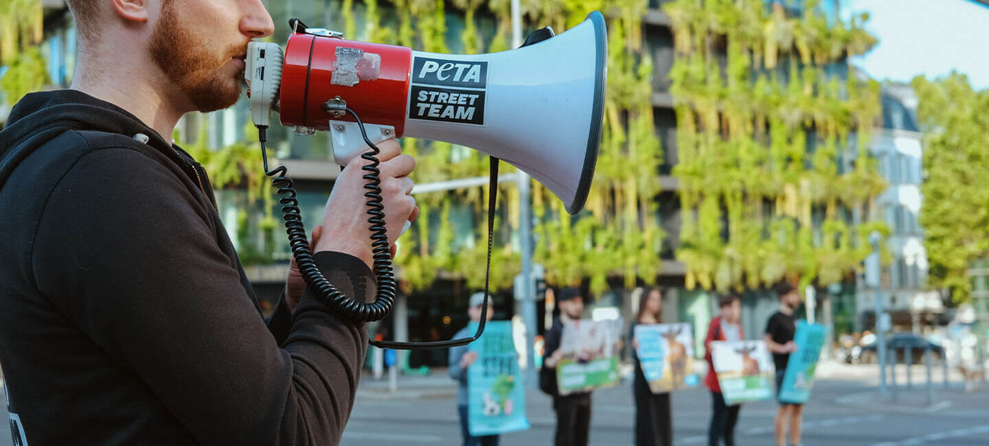 PETA Streetteam Demonstration auf der Strasse. Mann mit Megafon in der Hand.