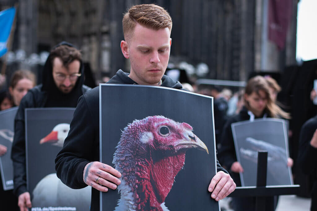 Mensch kniet vor dem Dom und hält Bild mit einem Huhn in der Hand