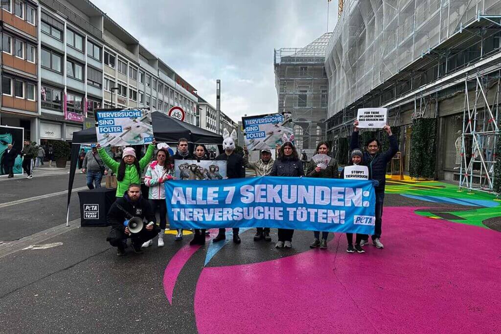 Menschen halten Protestschilder in der Hand und stehen vor einem blauen Banner