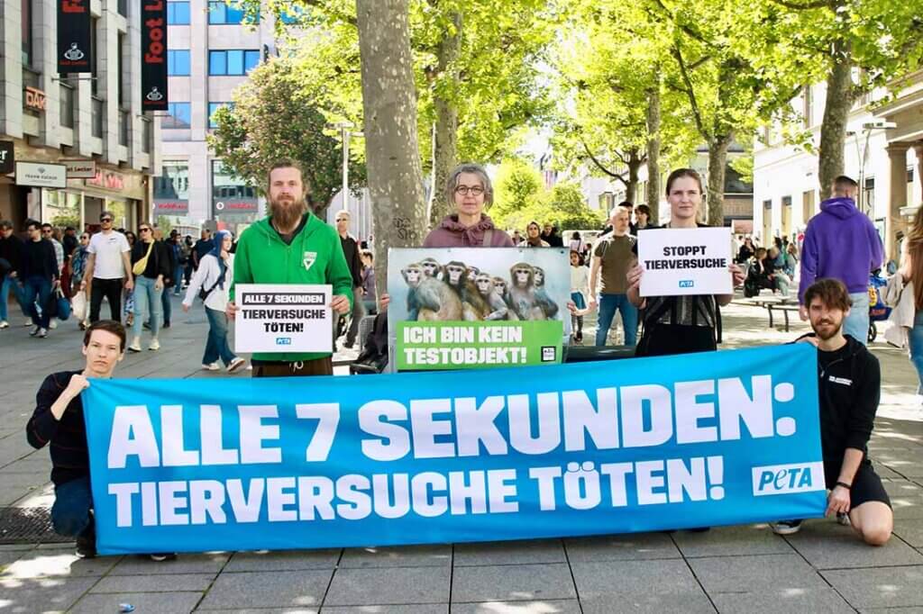 Menschen halten Protestschilder in der Hand und stehen vor einem blauen Banner