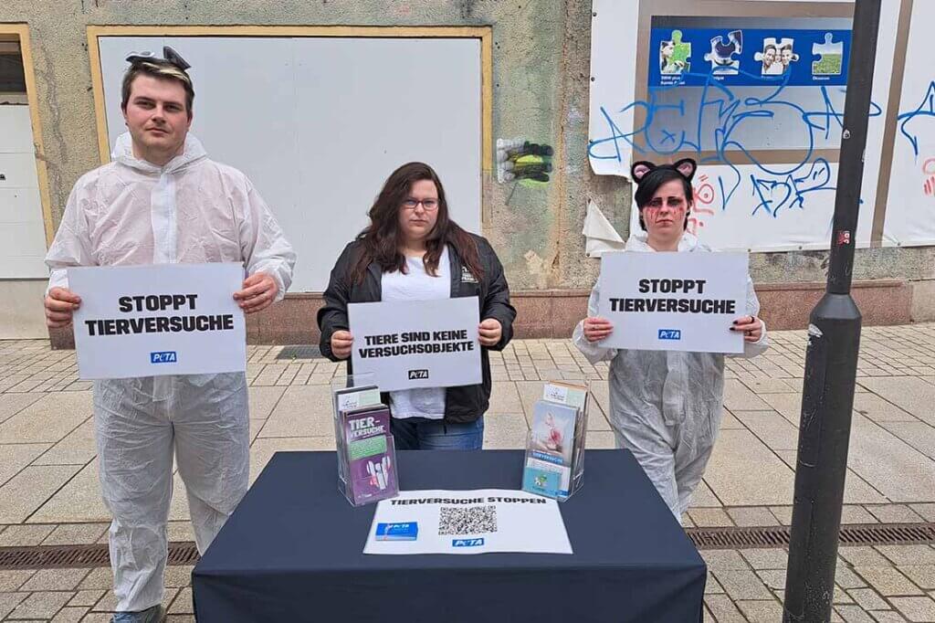 Menschen halten Protestschilder in der Hand und stehen hinter einem Stand