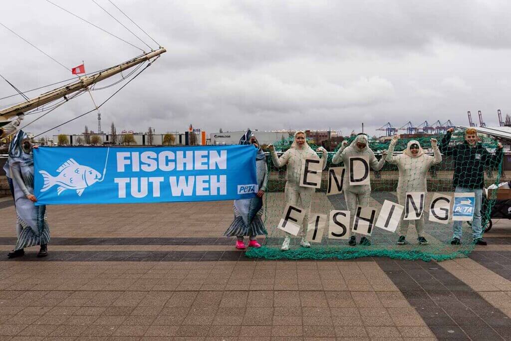 Aktion zum Welttag für das Ende der Fischerei vor einem Schiff im Hafen und Demonstrierende hinter einem Fischernetz.